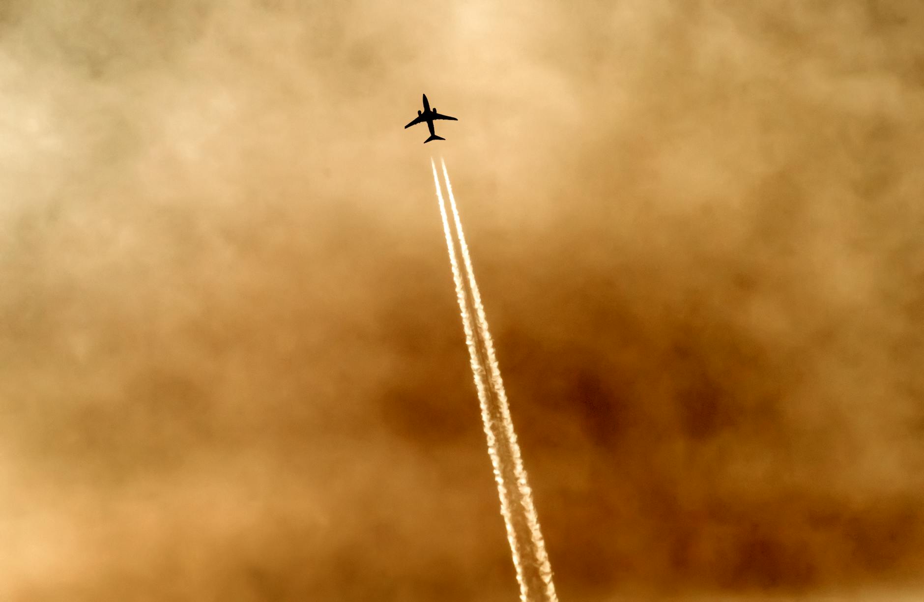 A striking silhouette of an airplane leaving contrails against a dramatic golden sky.