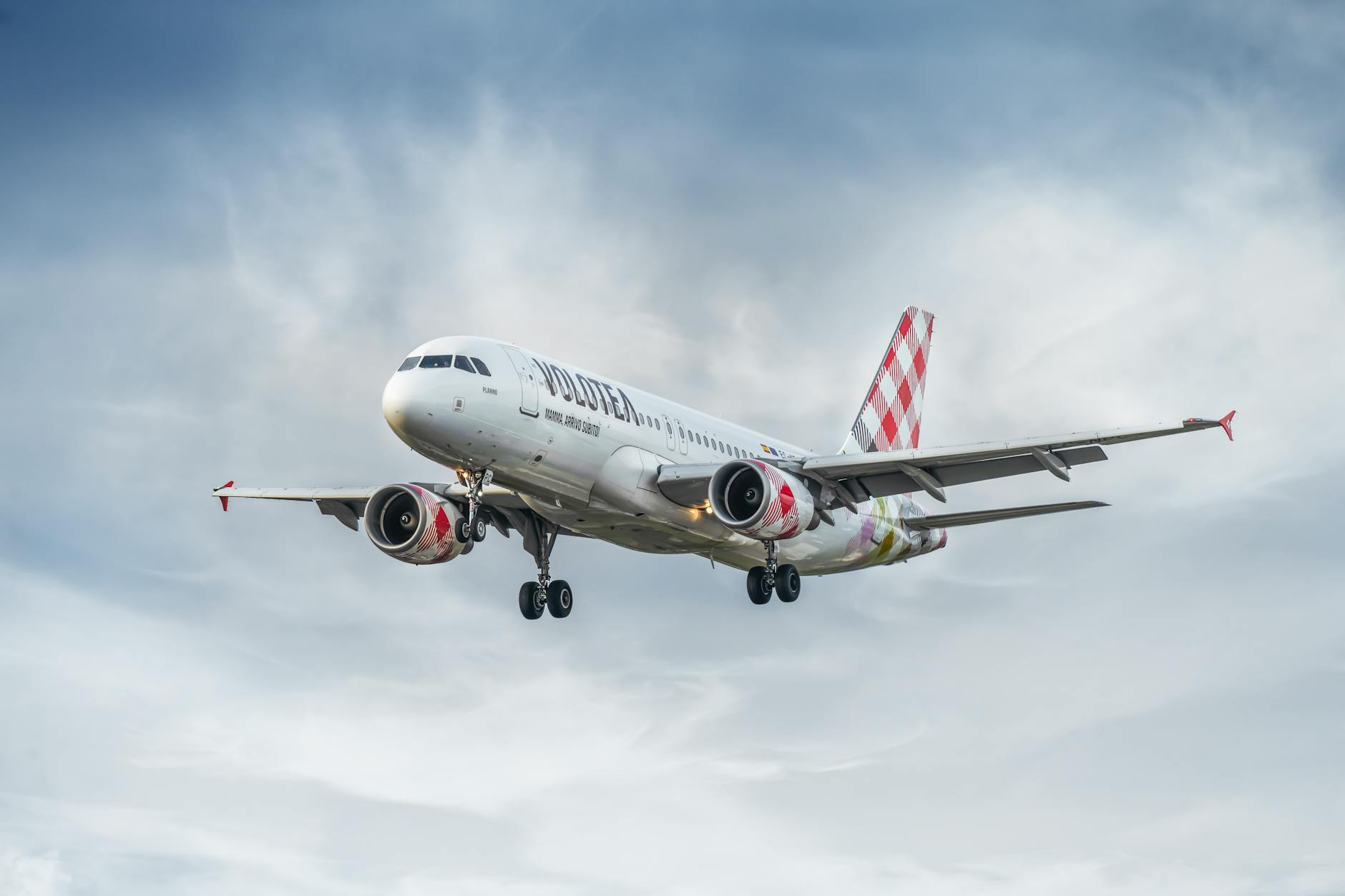 A Volotea commercial airplane flying through a cloudy sky, captured from below.