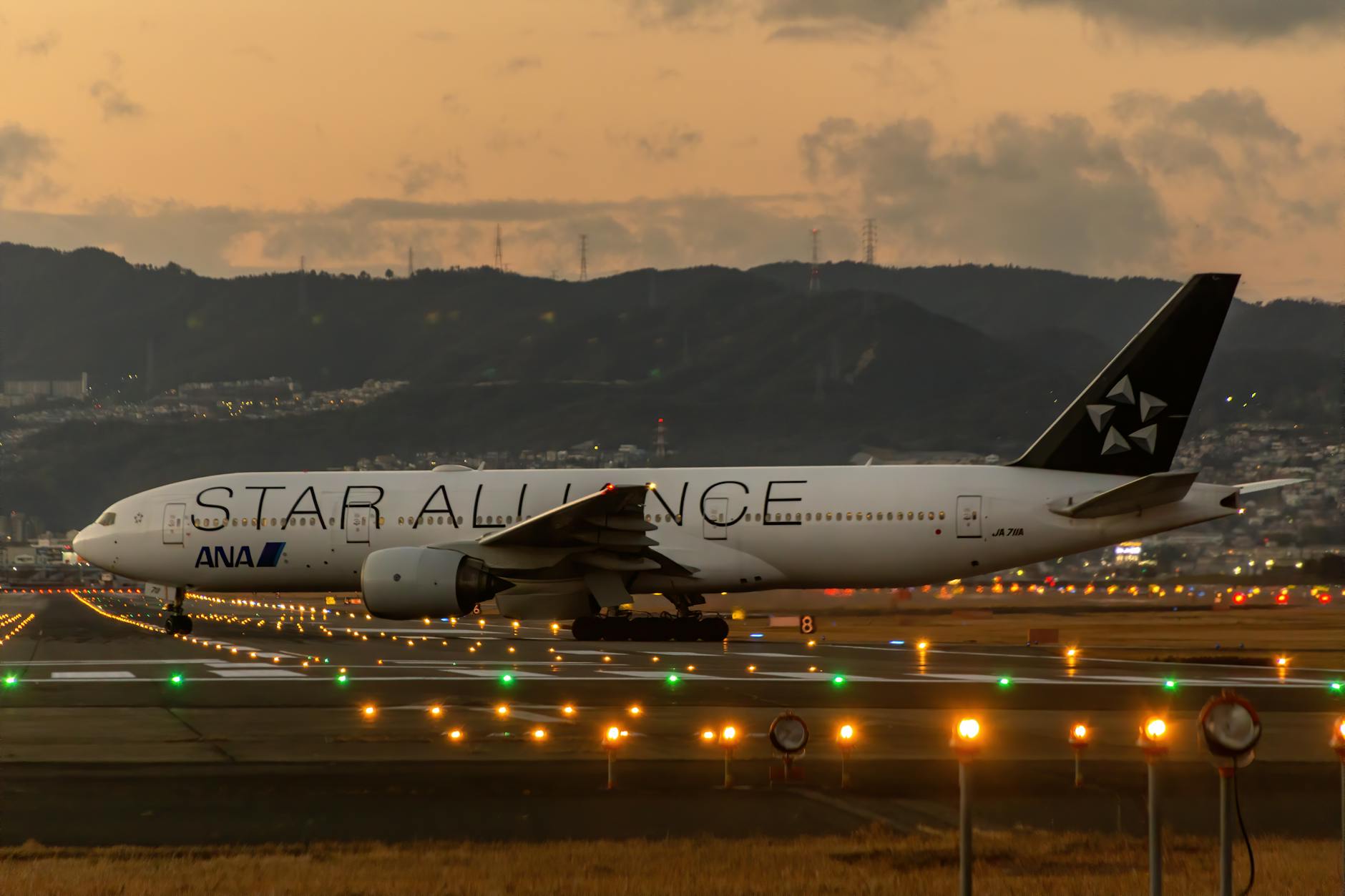 Star Alliance Boeing 777 landing at Osaka airport at dusk, capturing the vibrant runway lights and scenic backdrop.