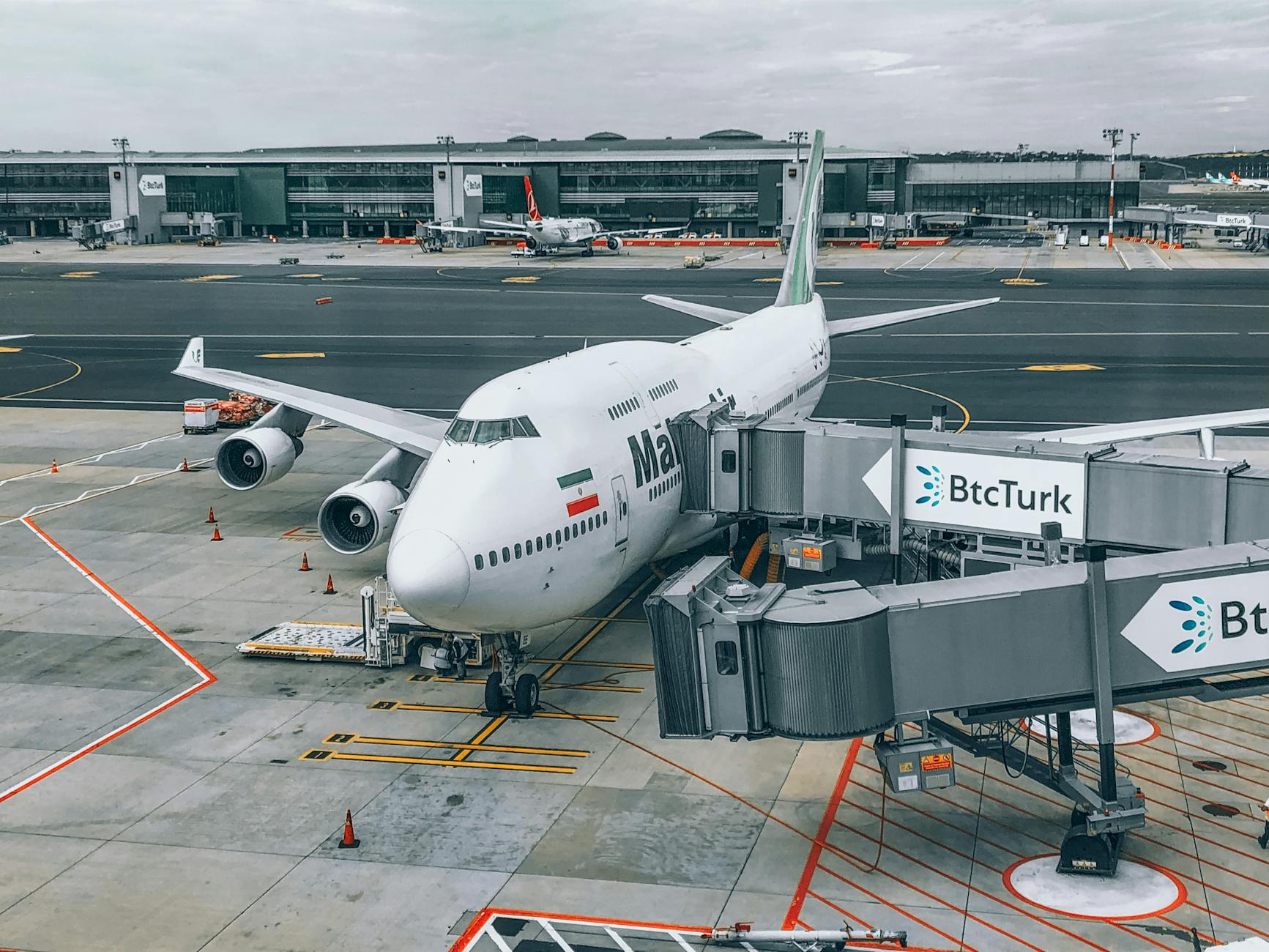 A Boeing 747 aircraft docked at the airport gate with visible jet bridge and terminal.