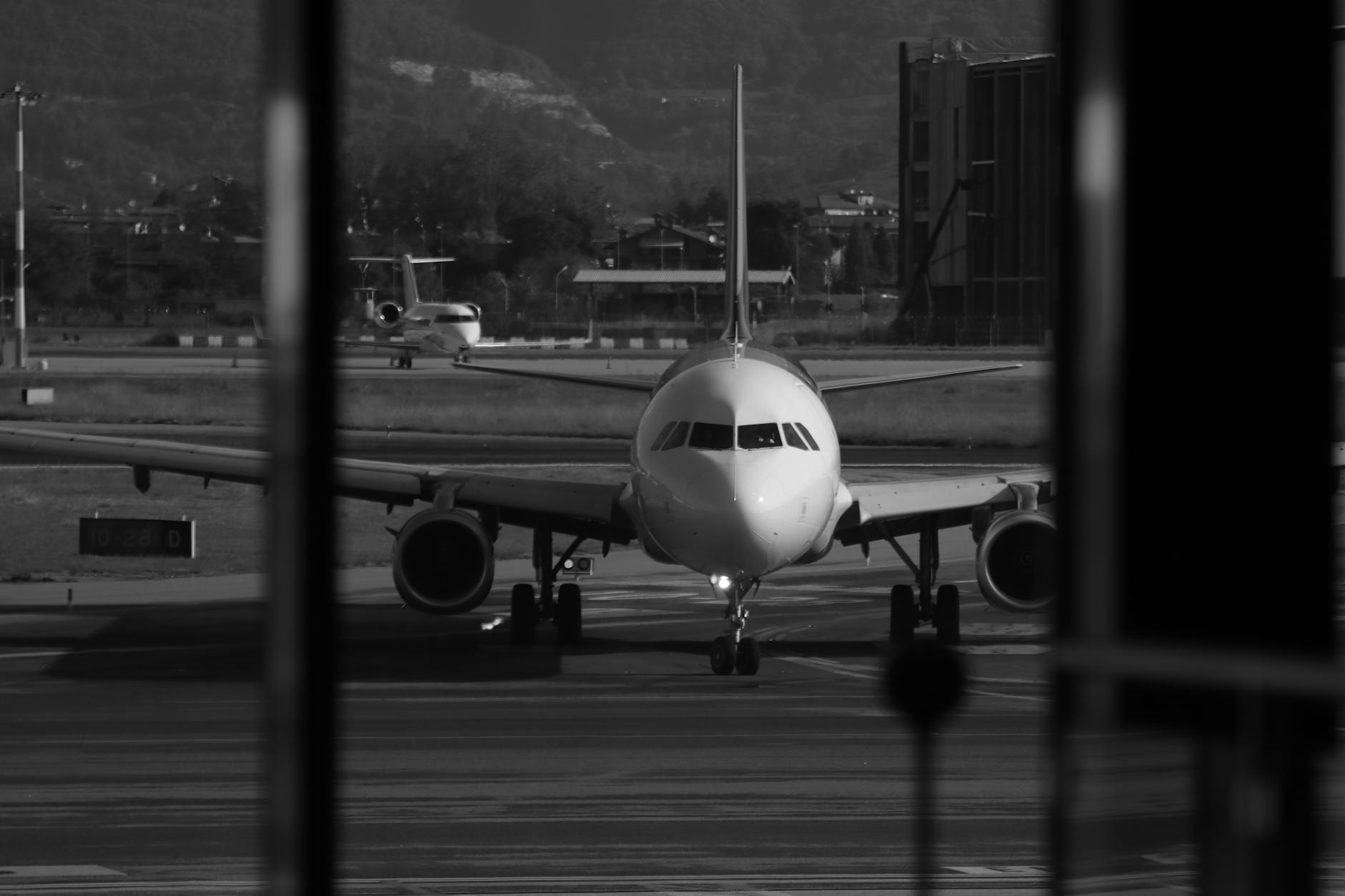 Artistic black and white photo of an airplane on the airport tarmac with mountains in the background.