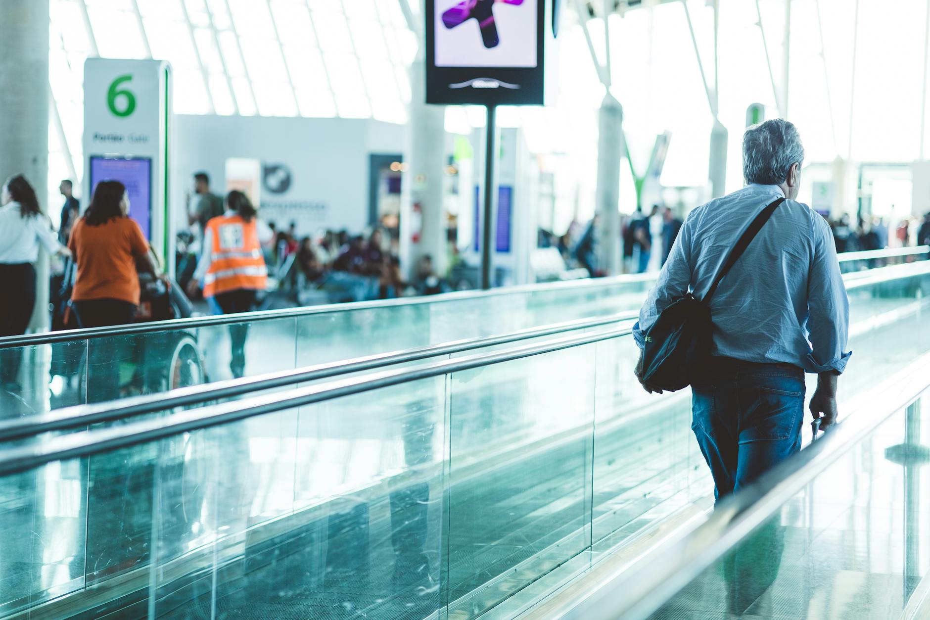 A bustling airport scene with travelers on a moving walkway in a modern terminal.