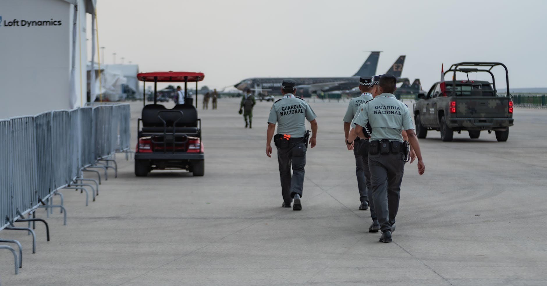 National Guard officers patrol a military airport, featuring aircraft and security vehicles.