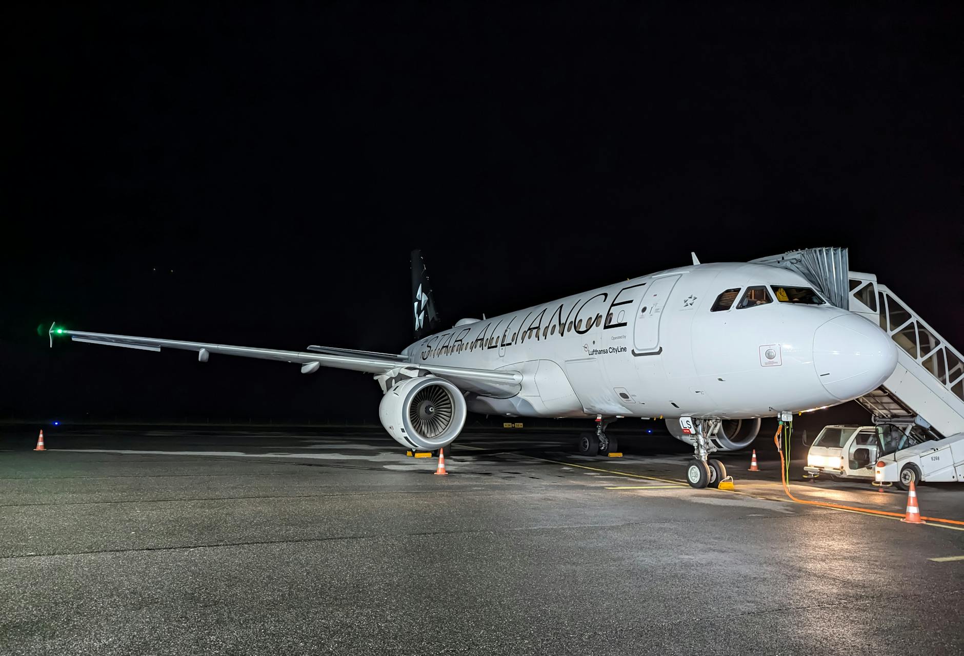 A commercial airplane with boarding stairs is ready for departure at night on an airport tarmac.