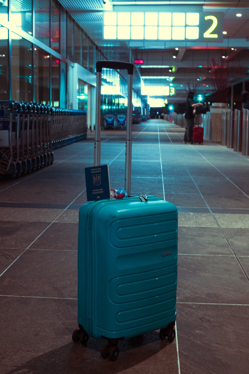 A blue suitcase with a passport in an empty airport terminal at night.