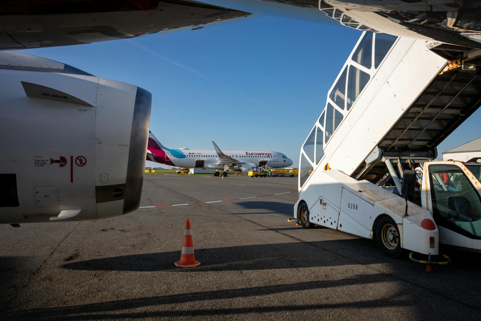 View of an airport tarmac featuring boarding stairs and an airplane in the background under a clear sky.