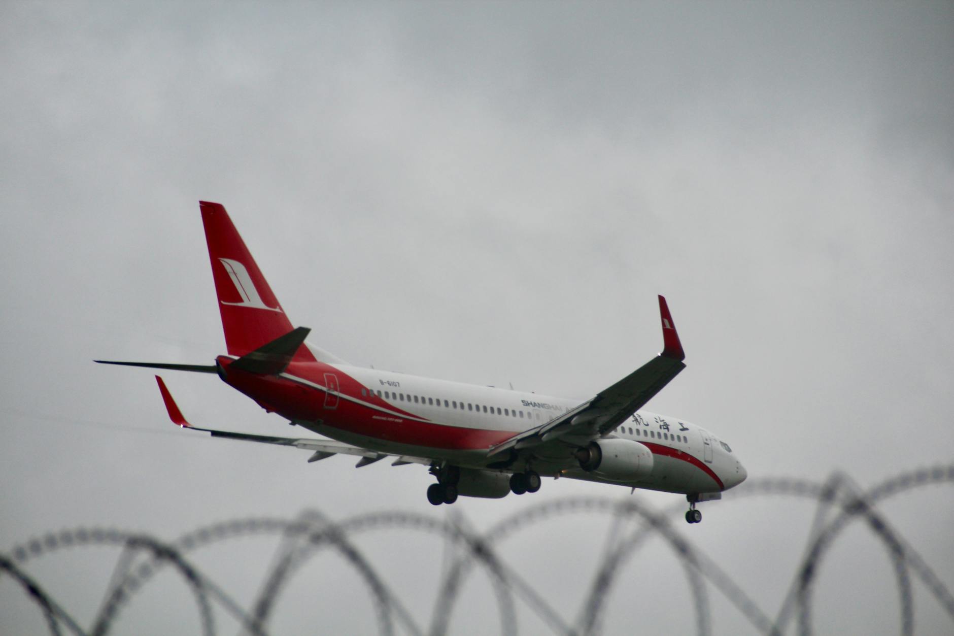 A commercial airplane approaches landing with barbed wire visible, symbolizing travel and security.