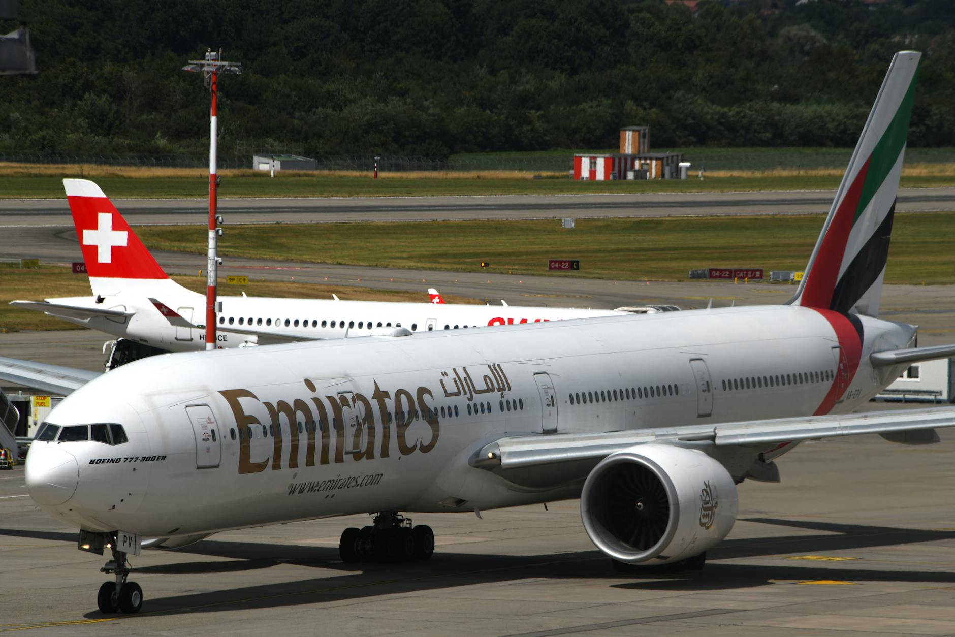 Emirates Boeing 777-300ER taxiing at Geneva Airport with Swiss aircraft in background.