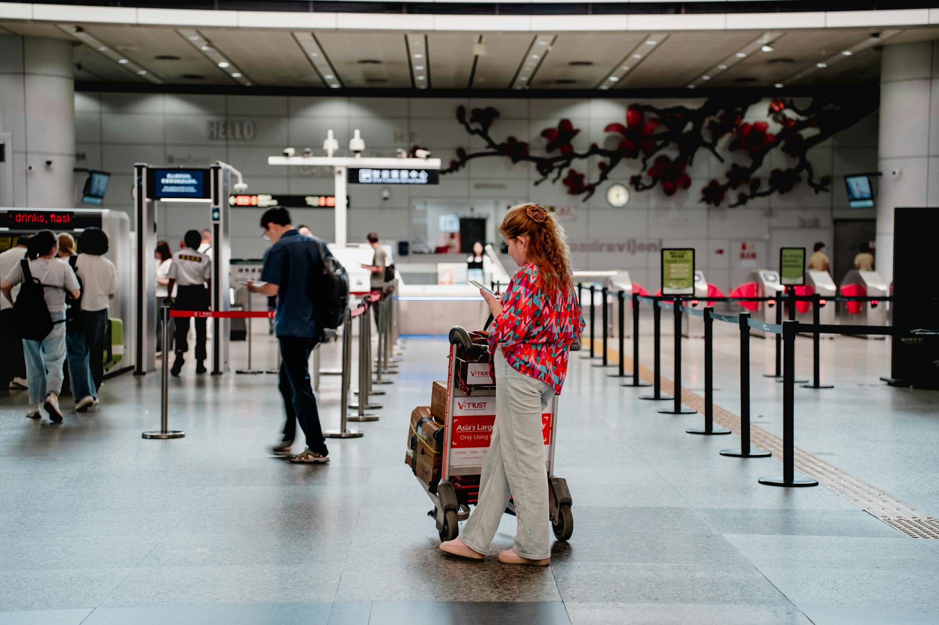 A traveler checks her phone while waiting with a luggage cart at a busy airport terminal in Guangzhou.