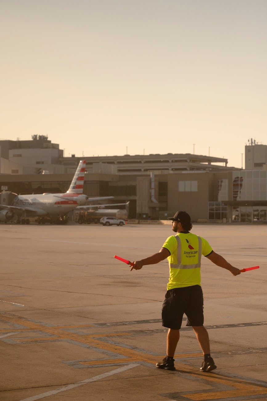 An airport worker signals an aircraft on the tarmac at sunset.