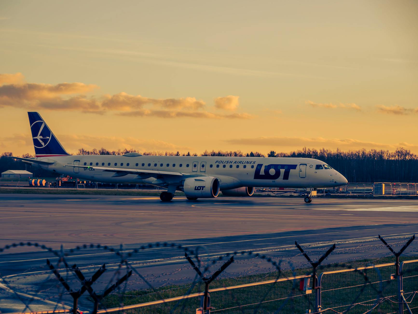 A LOT Polish Airlines plane taxies on a runway at Wrocław Airport during sunset.