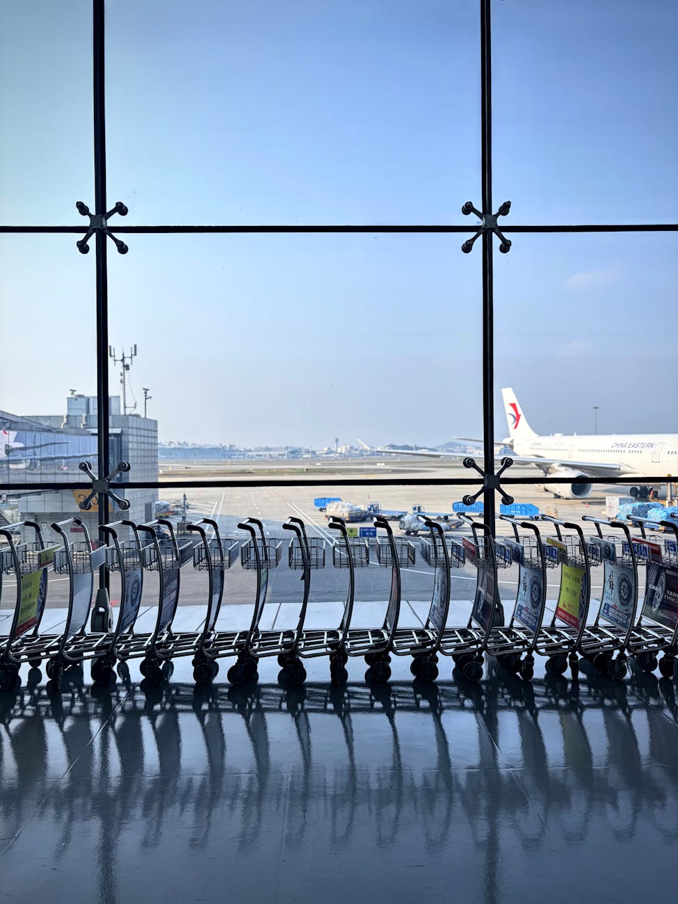 Airport scene with lined trolleys and airplane at a sunny terminal window.
