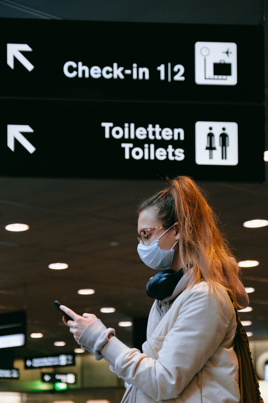 Woman wearing a face mask checks her phone at an airport during pandemic times.