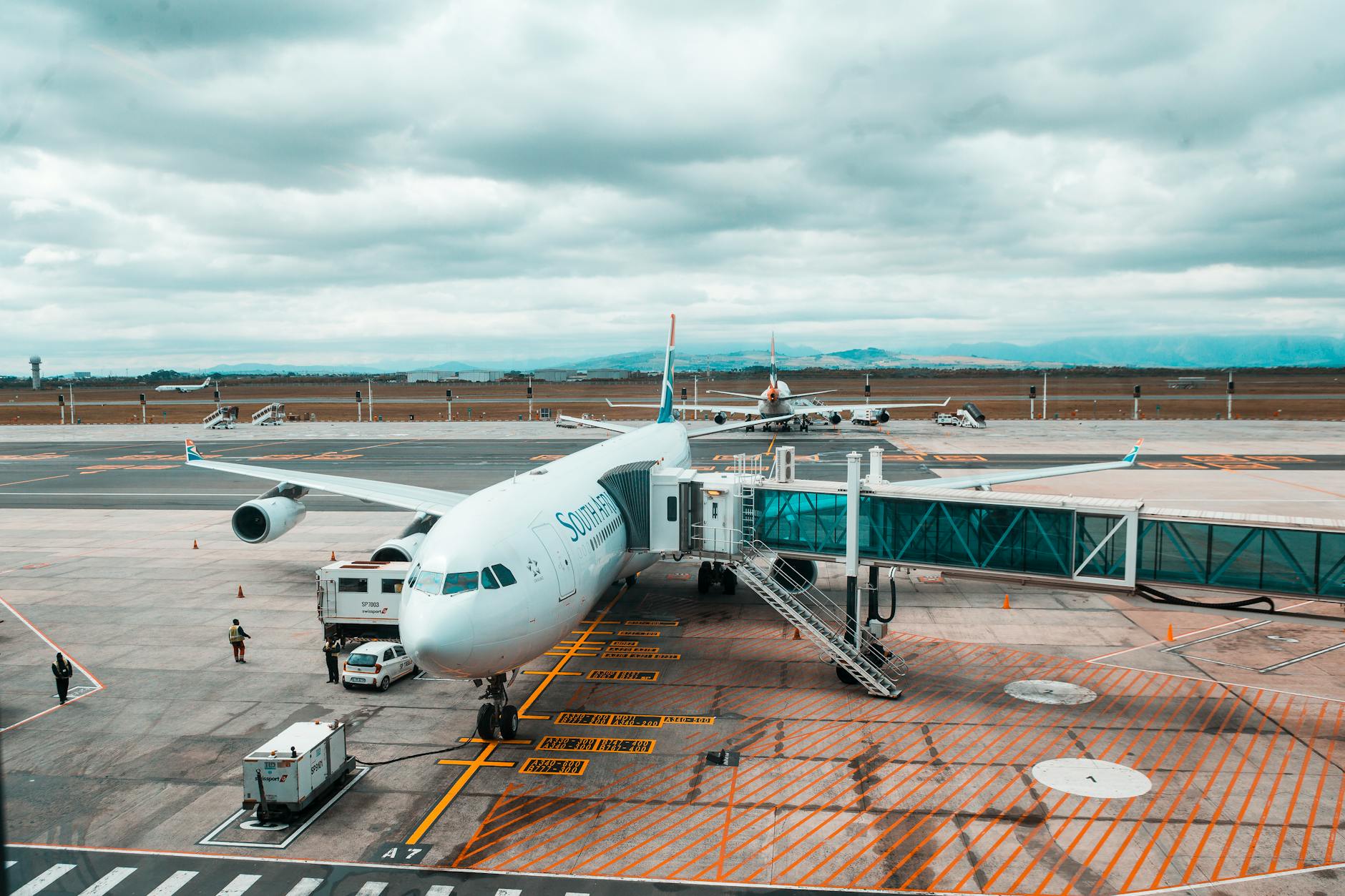 A large commercial airplane connected to a jet bridge at a South African airport terminal.