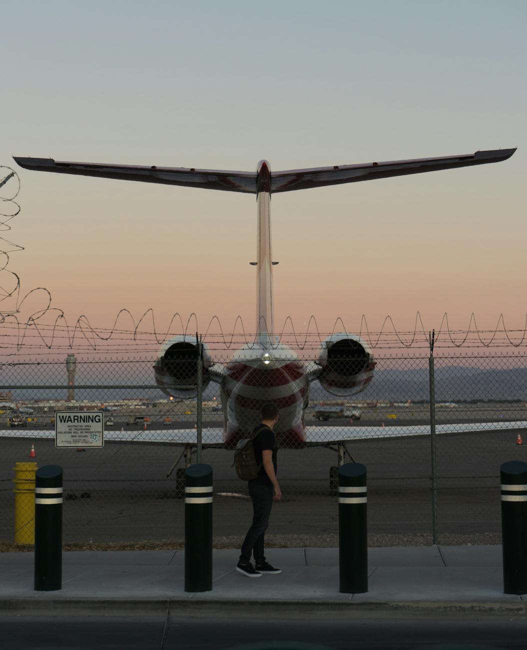 A traveler at airport fence watching a plane during dusk in Las Vegas.