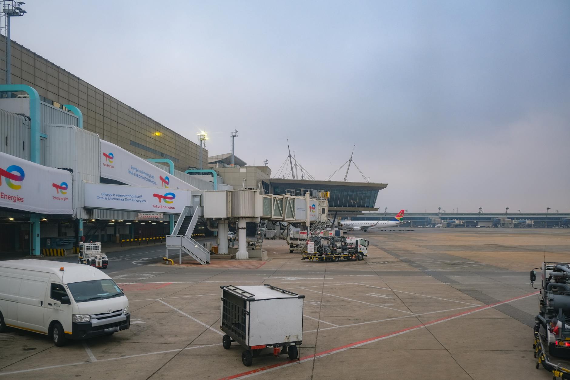 View of an airport apron showcasing vehicles, tarmac, and gates on a cloudy day.