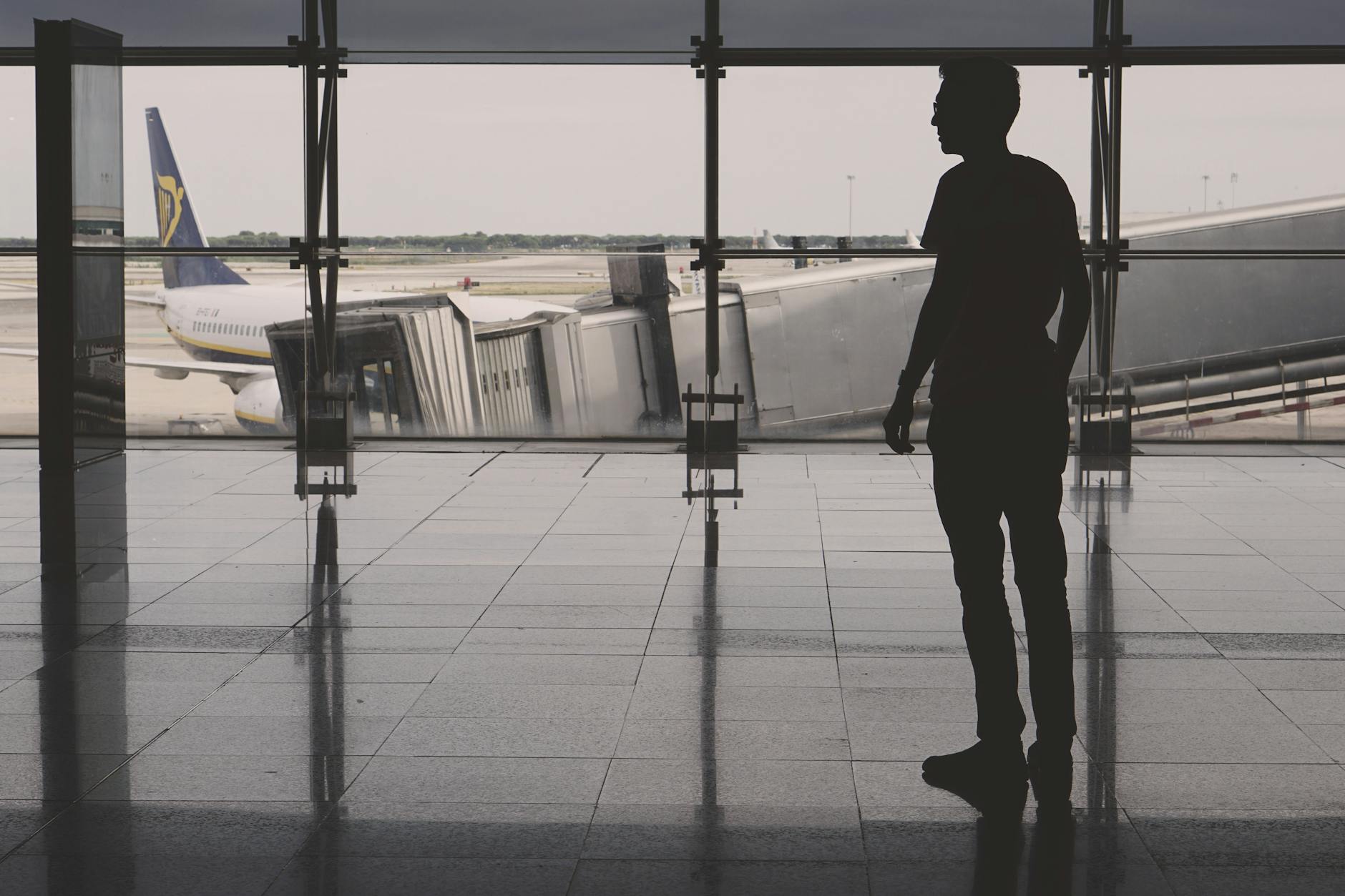 Silhouette of a man at El Prat airport with airplane reflections on glass walls.