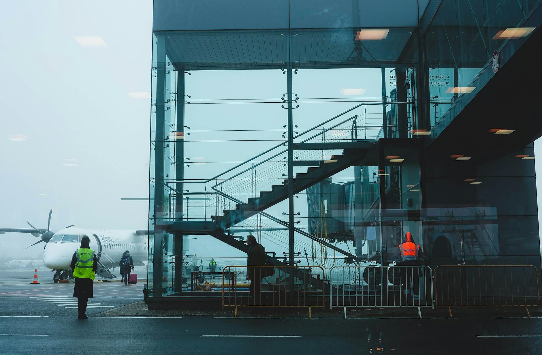 Passengers boarding an airplane at Riga Airport amidst fog, showcasing modern airport architecture.