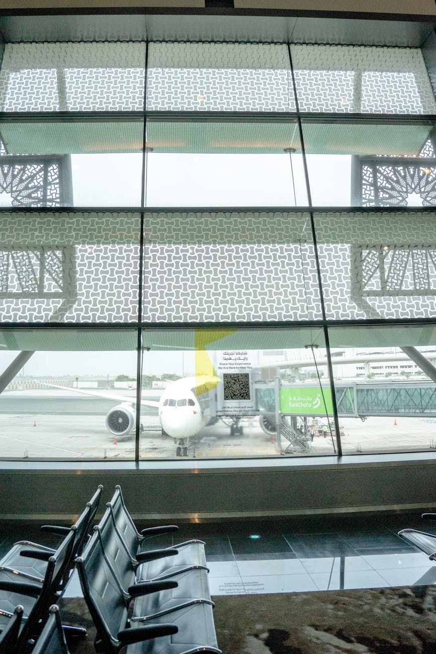 Interior view of airport terminal with aircraft on tarmac beyond glass windows.