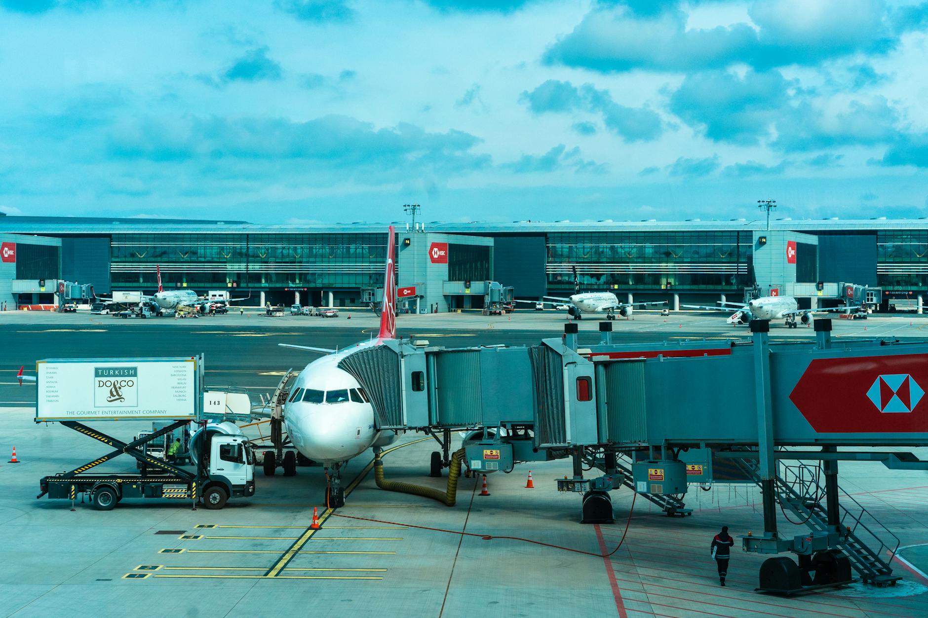 Airplane at gate with jetway and loading trucks at a bustling airport.