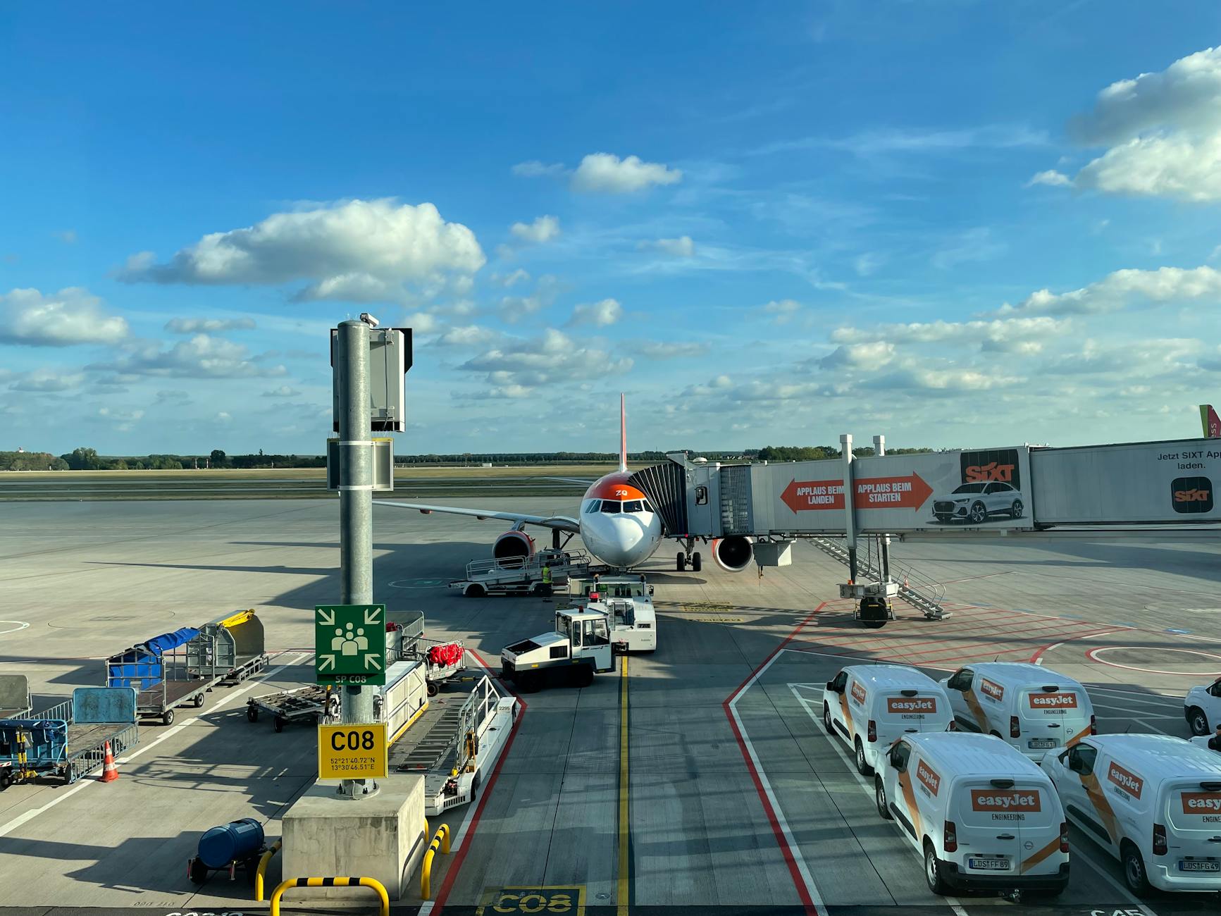 EasyJet airplane stationed at Schönefeld Airport gate with support vehicles surrounding.