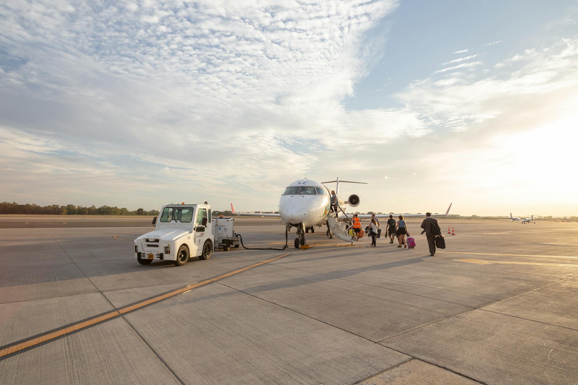 Travelers board an airplane on the tarmac under a bright sky at the airport.