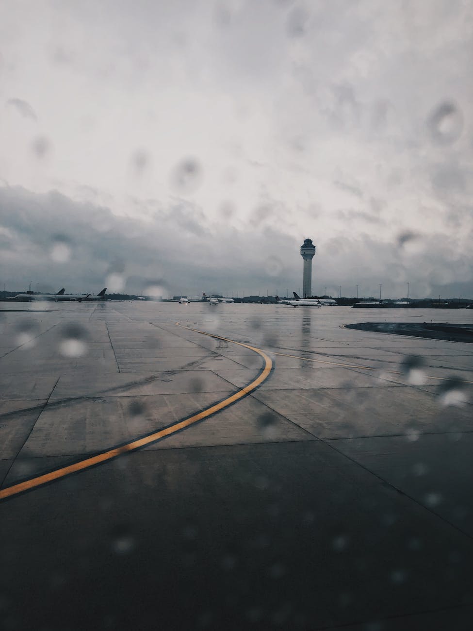 Raindrops on window overlooking airport runway and control tower under cloudy sky.