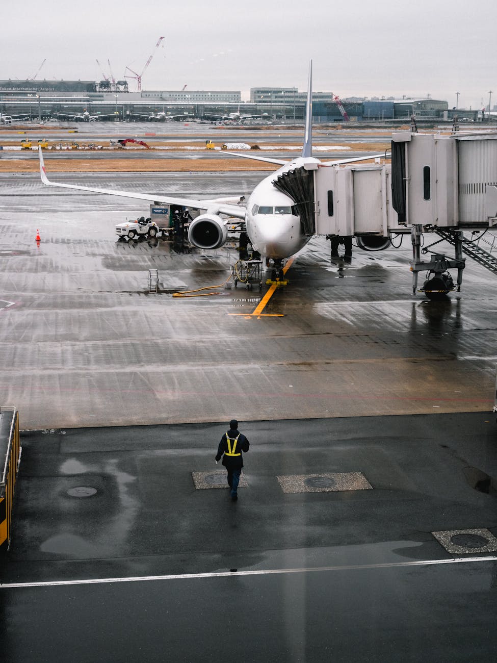Airplane parked at airport gate on a rainy day with a ground crew member walking.