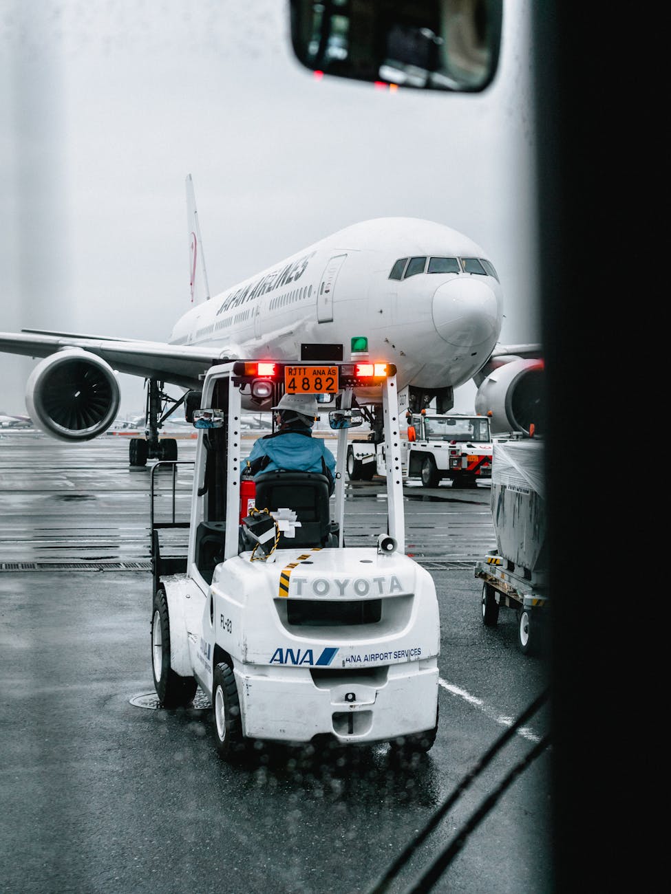 Airport ground crew operating a vehicle in front of a parked airliner on a rainy runway.