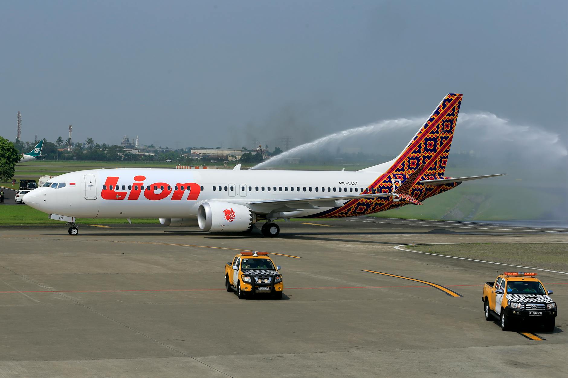 Lion Air airplane receiving a water salute on an airport runway, with utility vehicles nearby.