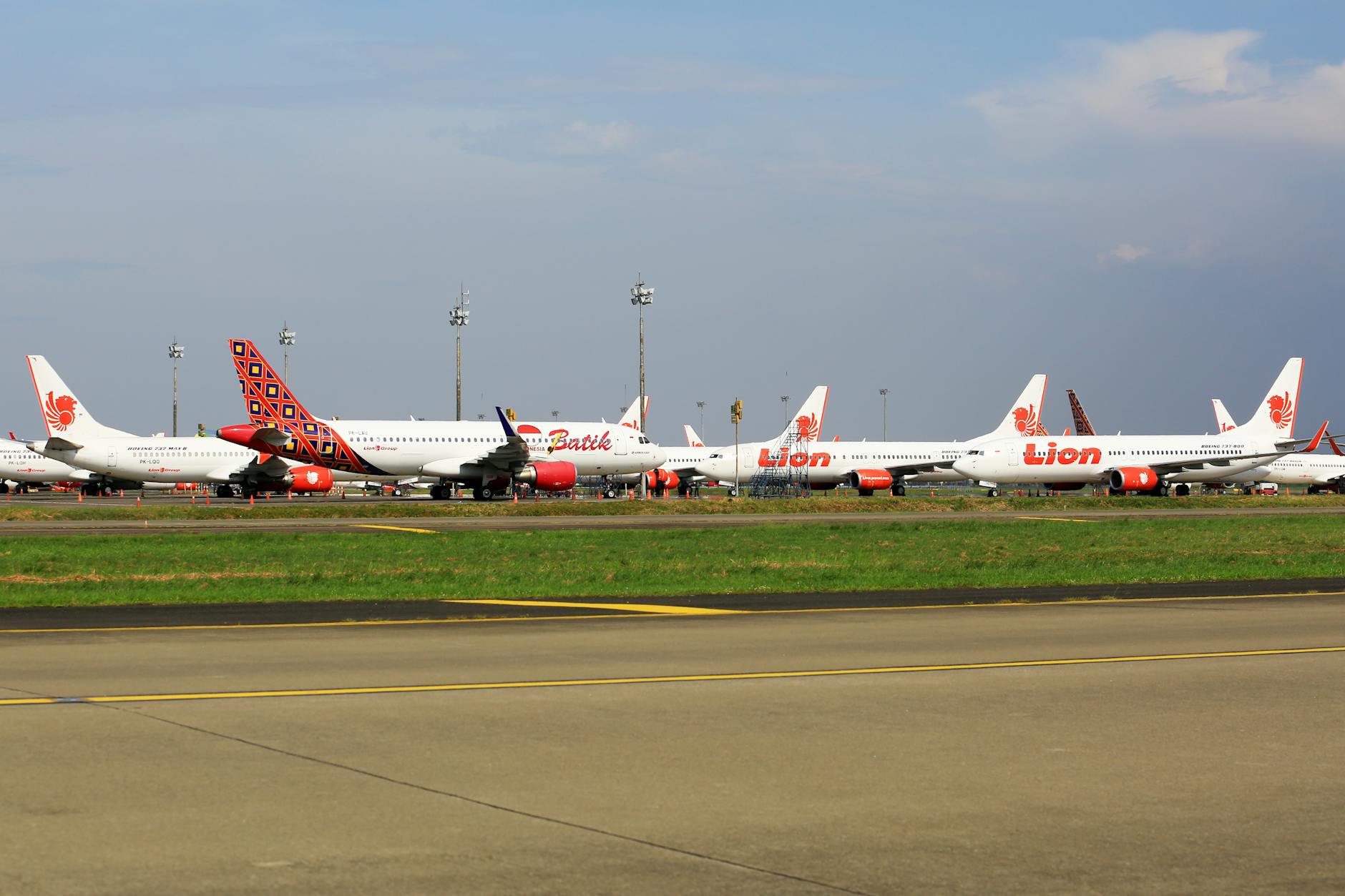Multiple airplanes from Lion Air parked on an airport runway, ready for takeoff.