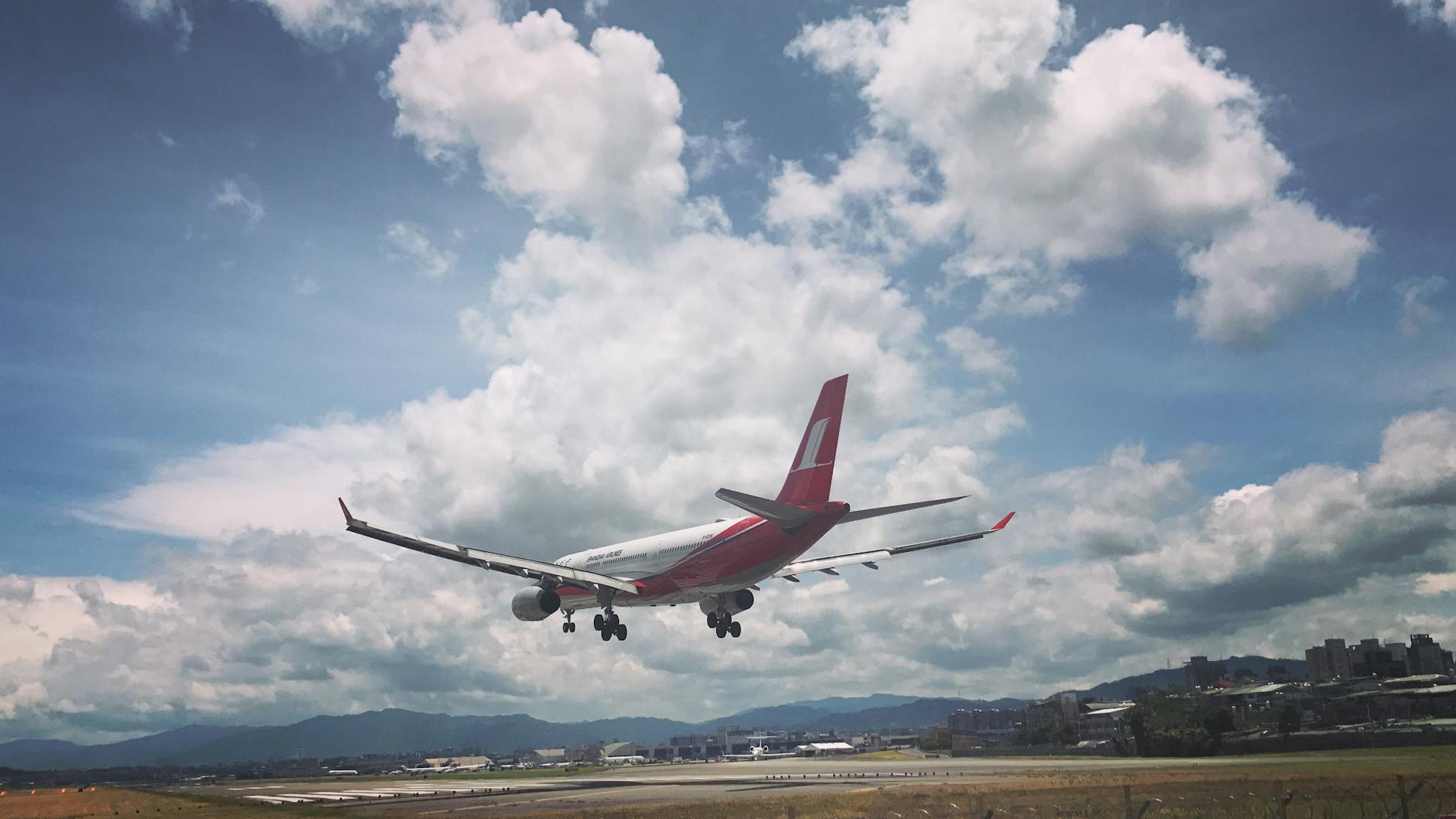 A commercial airplane approaches landing at Taipei's airport under a partly cloudy sky.