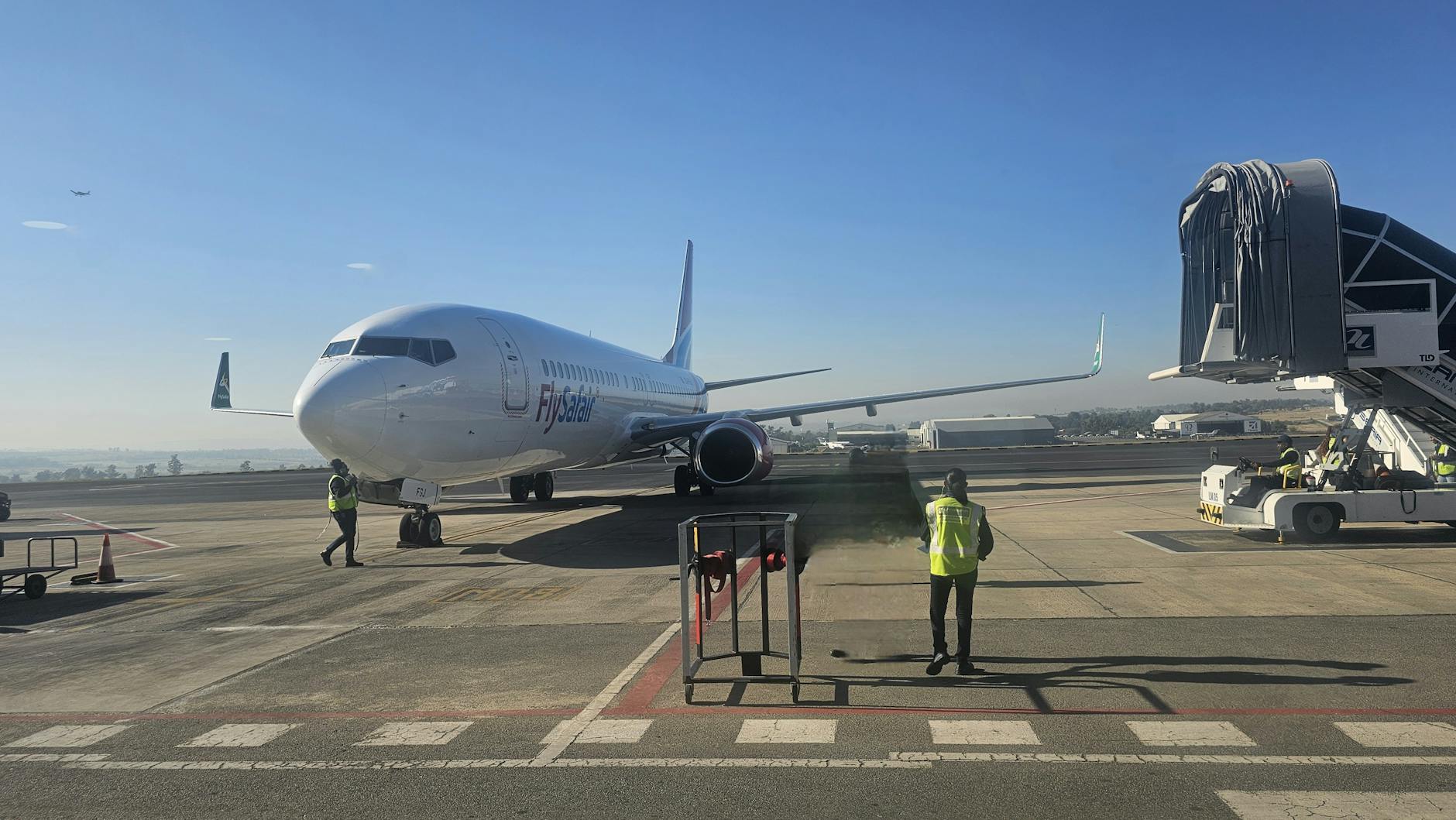 A commercial airplane on the runway with ground staff preparing for departure.