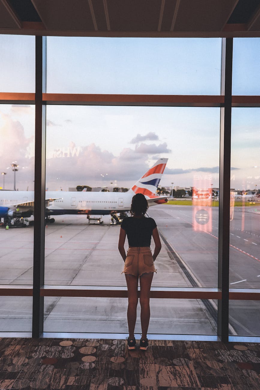 A woman stands at a glass window viewing airplanes at Singapore Airport, capturing the essence of travel and anticipation.