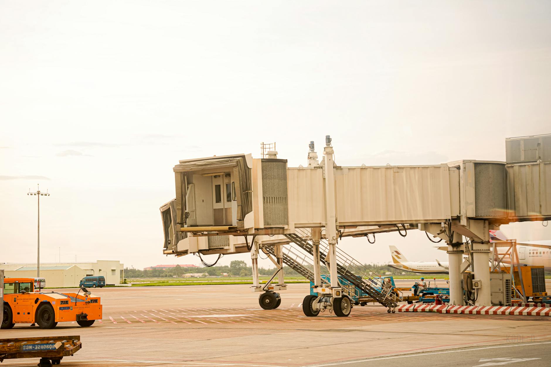 Wide view of an airport jet bridge and apron under clear daylight, featuring ground support equipment.