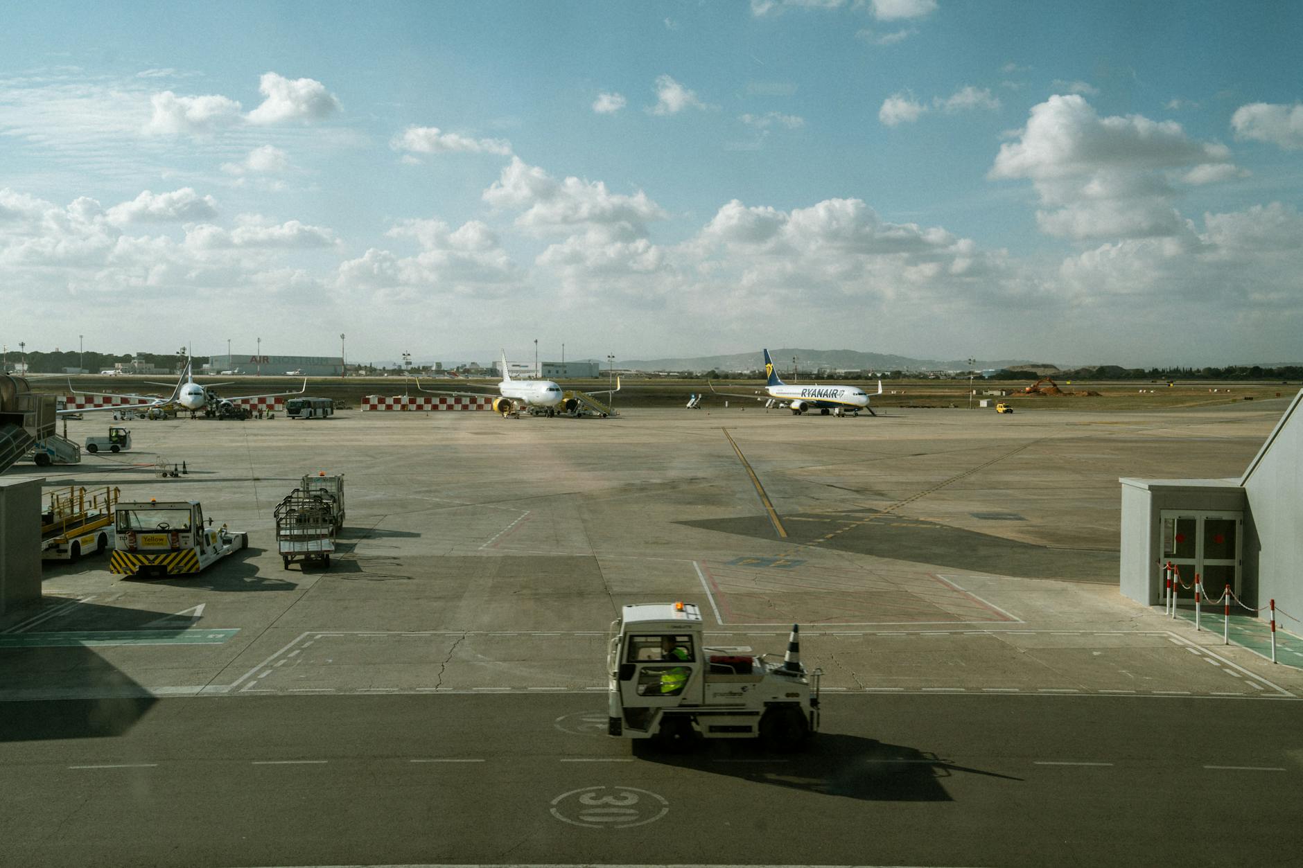 Wide view of an airport tarmac with multiple airplanes and ground vehicles under a cloudy sky.