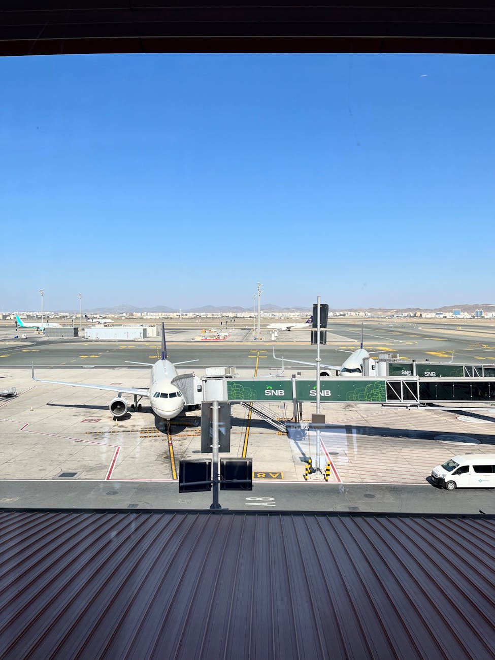 Airplane docked at terminal gate in Jeddah Airport, clear blue sky.