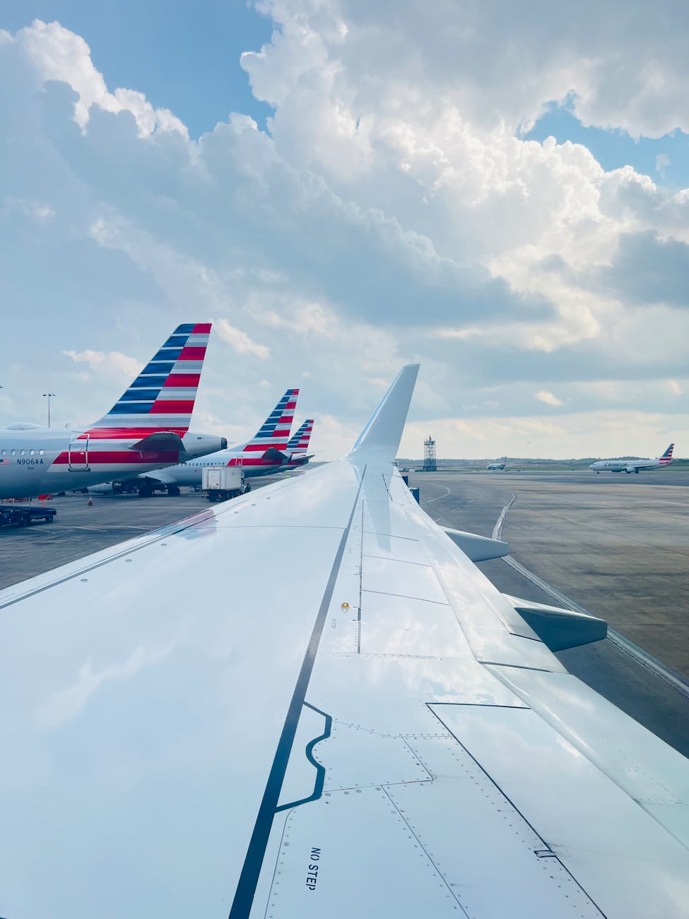 View of airplane wing at Charlotte Airport with cloudy sky and aircrafts on the ground.