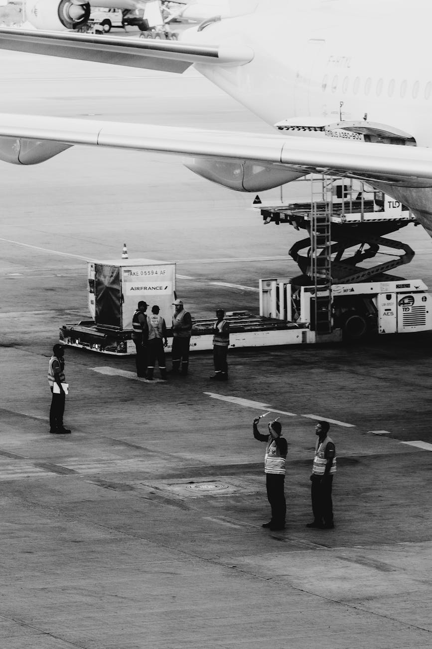 Black and white image of airline ground crew coordinating luggage loading at an airport