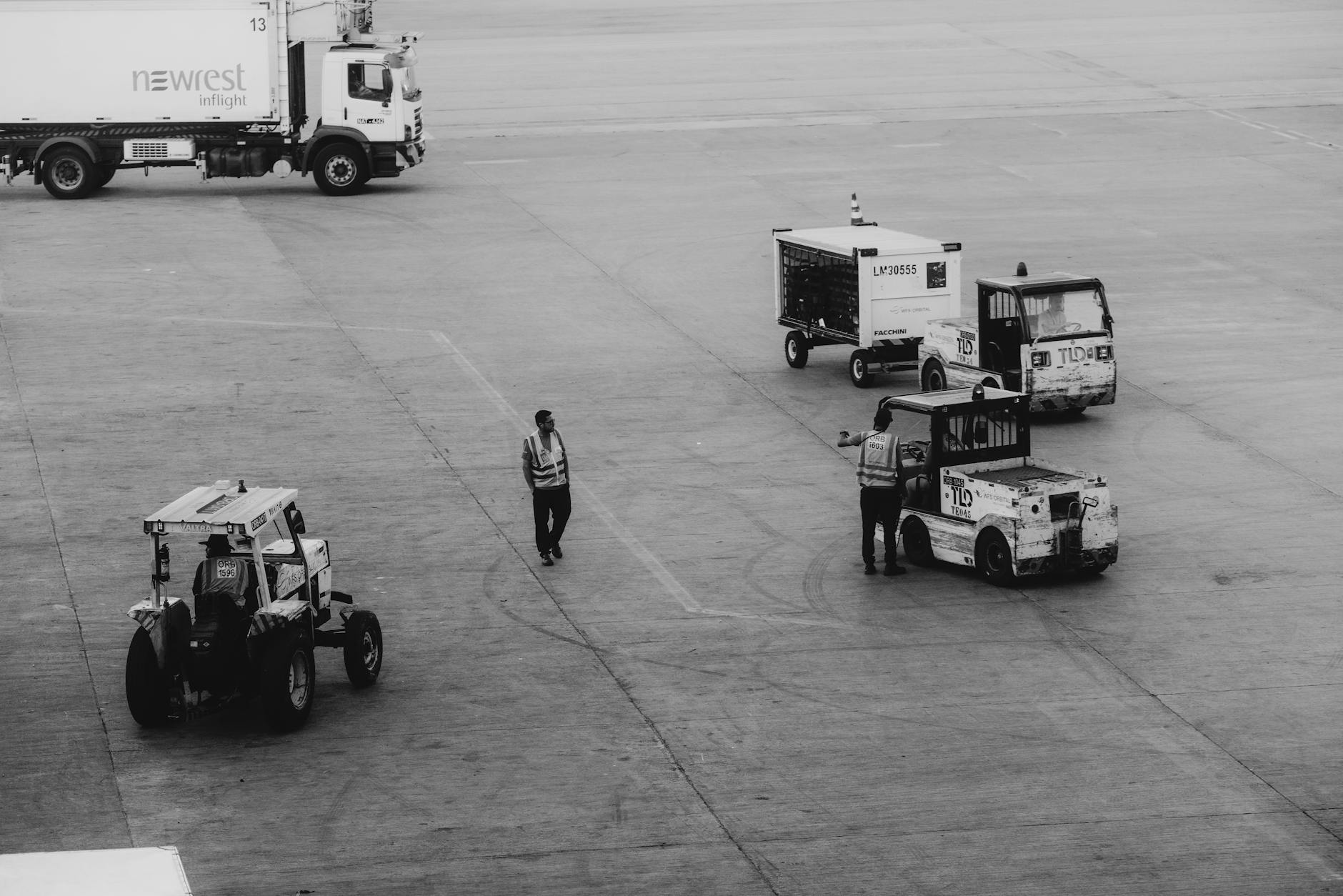 Black and white image of airport ground crew managing service vehicles on the tarmac.
