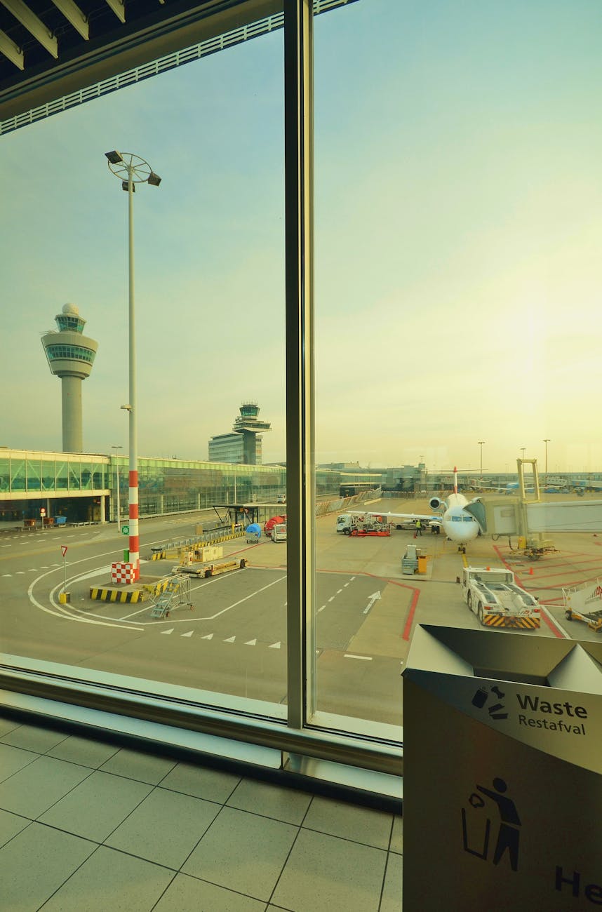 Perspective of airport runway and airplane seen from terminal window during day.