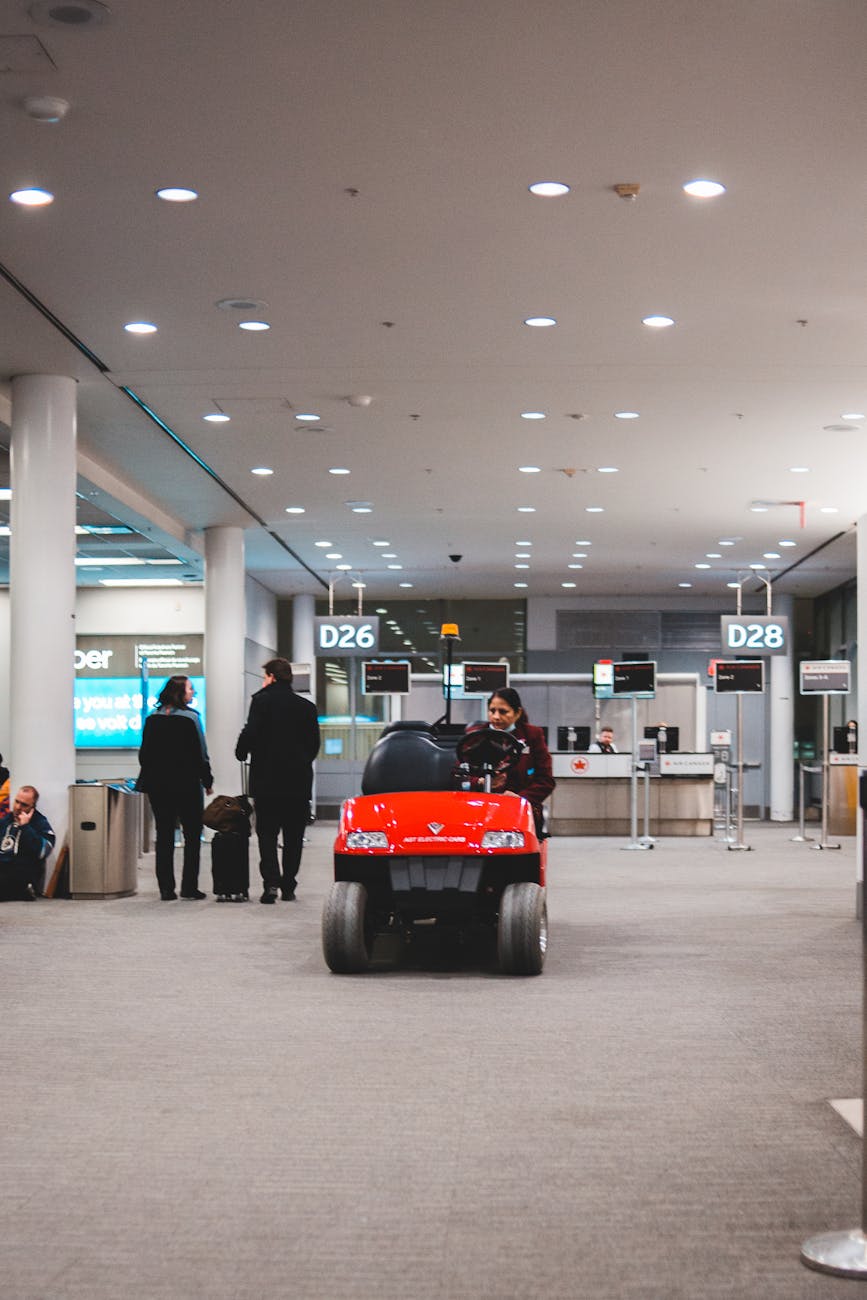 A red electric vehicle drives through an airport terminal near boarding gate D26.