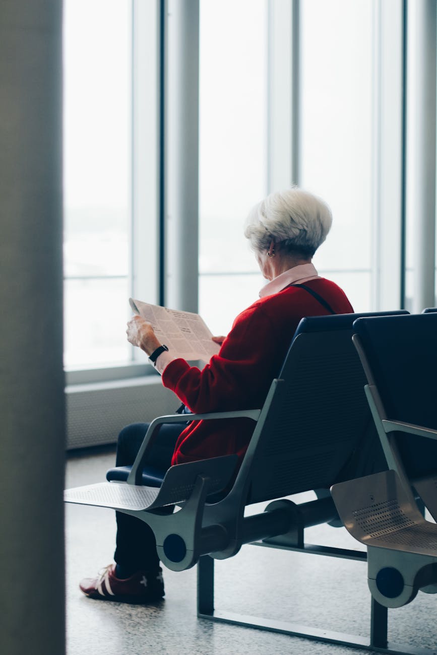 Elderly woman reading newspaper while seated at an airport gate.