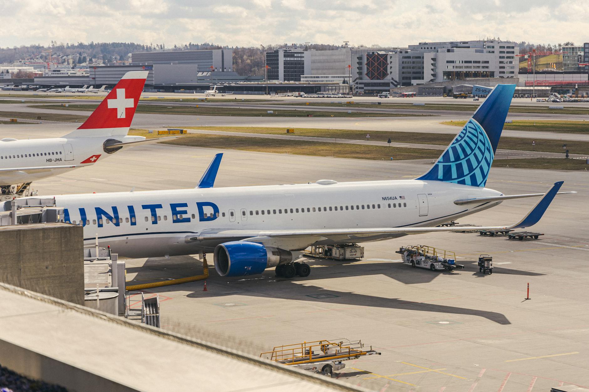 United Airlines and Swiss planes parked at Zurich airport terminal on a clear day.