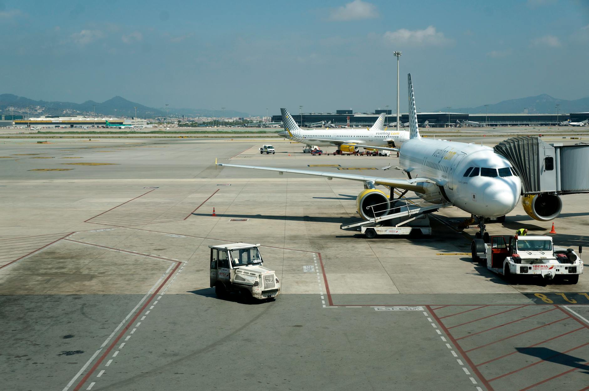 A commercial airplane prepares for boarding at Girona Airport with clear skies and mountains in the distance.