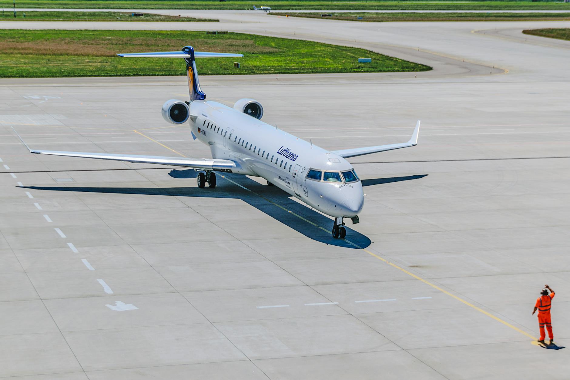 A Lufthansa airplane on the runway with an airport staff member directing traffic.