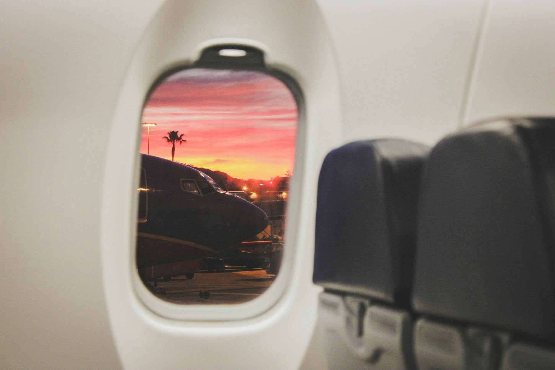 Scenic sunset view through airplane window with plane and palm silhouettes on tarmac.