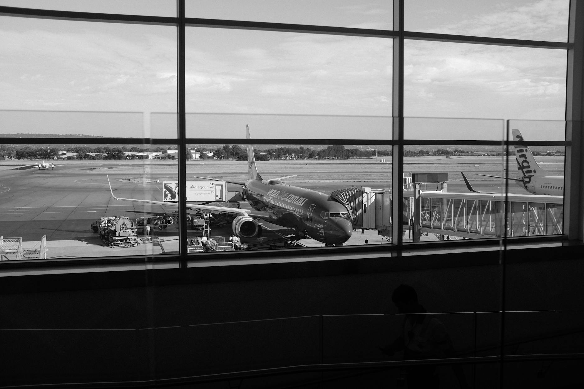 Monochrome view of an airport runway showcasing airplanes and gates through large windows.