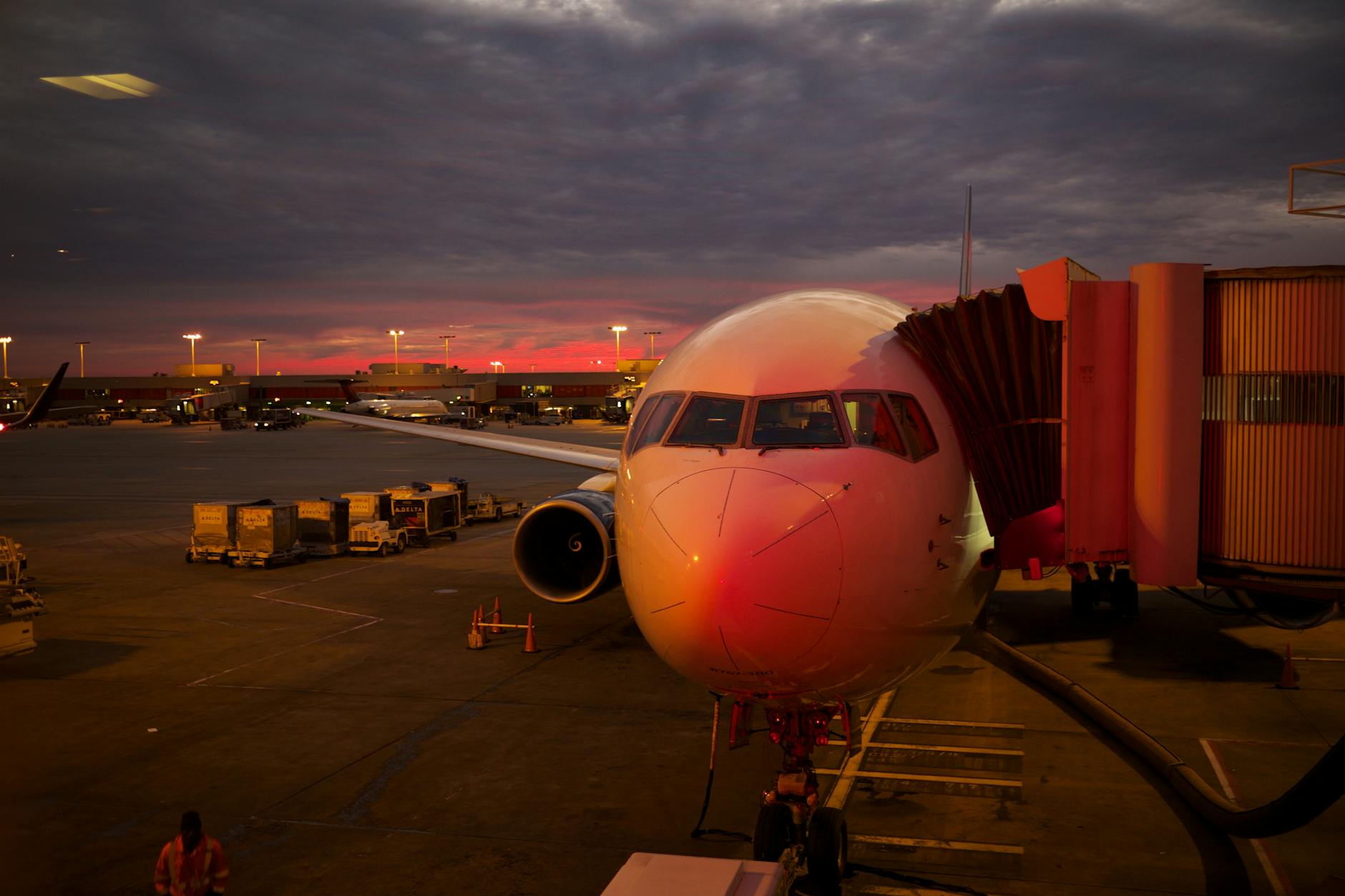 Plane boarding at sunset with vibrant sky colors and airport lights.