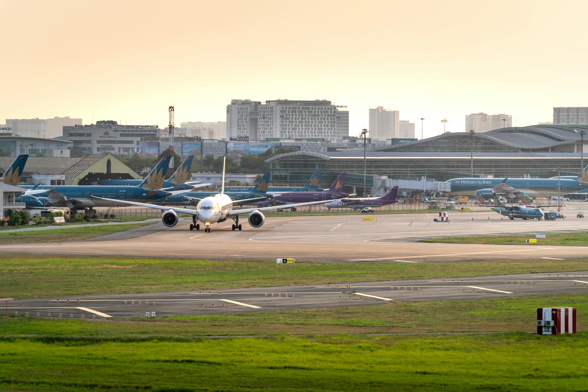 A bustling airport scene with multiple airplanes and a cityscape backdrop at sunset.